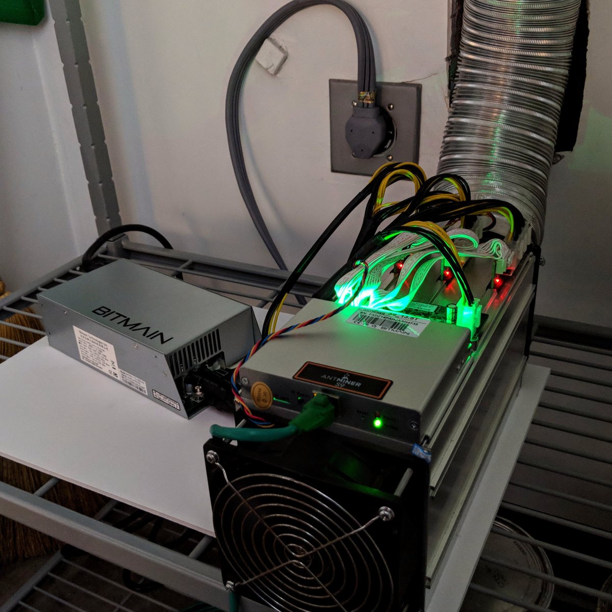An open bitcoin mining machine showing rows of chips under heatsinks and two large fans.
