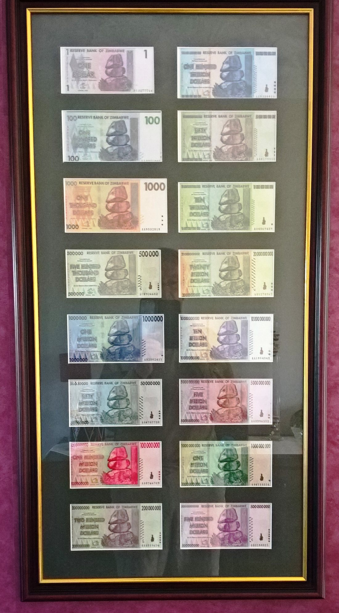 Sixteen Zimbabwean banknotes laid out in a grid, running from one dollar up to one hundred trillion dollars.