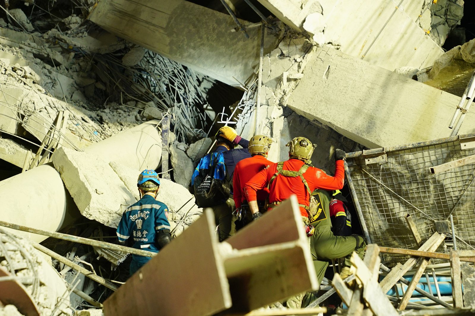 Rescue workers in helmets beside the rubble of the collapsed State Audit Office tower in Bangkok
