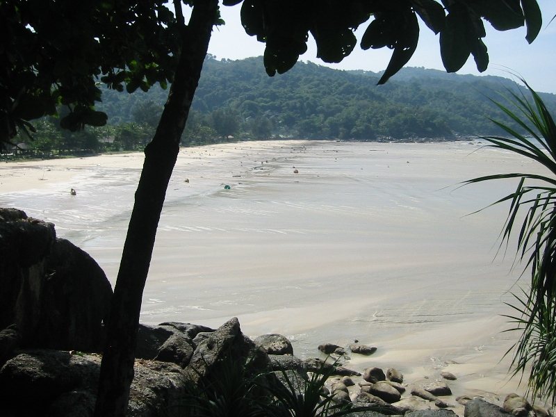 Kata Noi beach, Phuket, with the sea pulled far back, leaving wide wet sand and small boats stranded