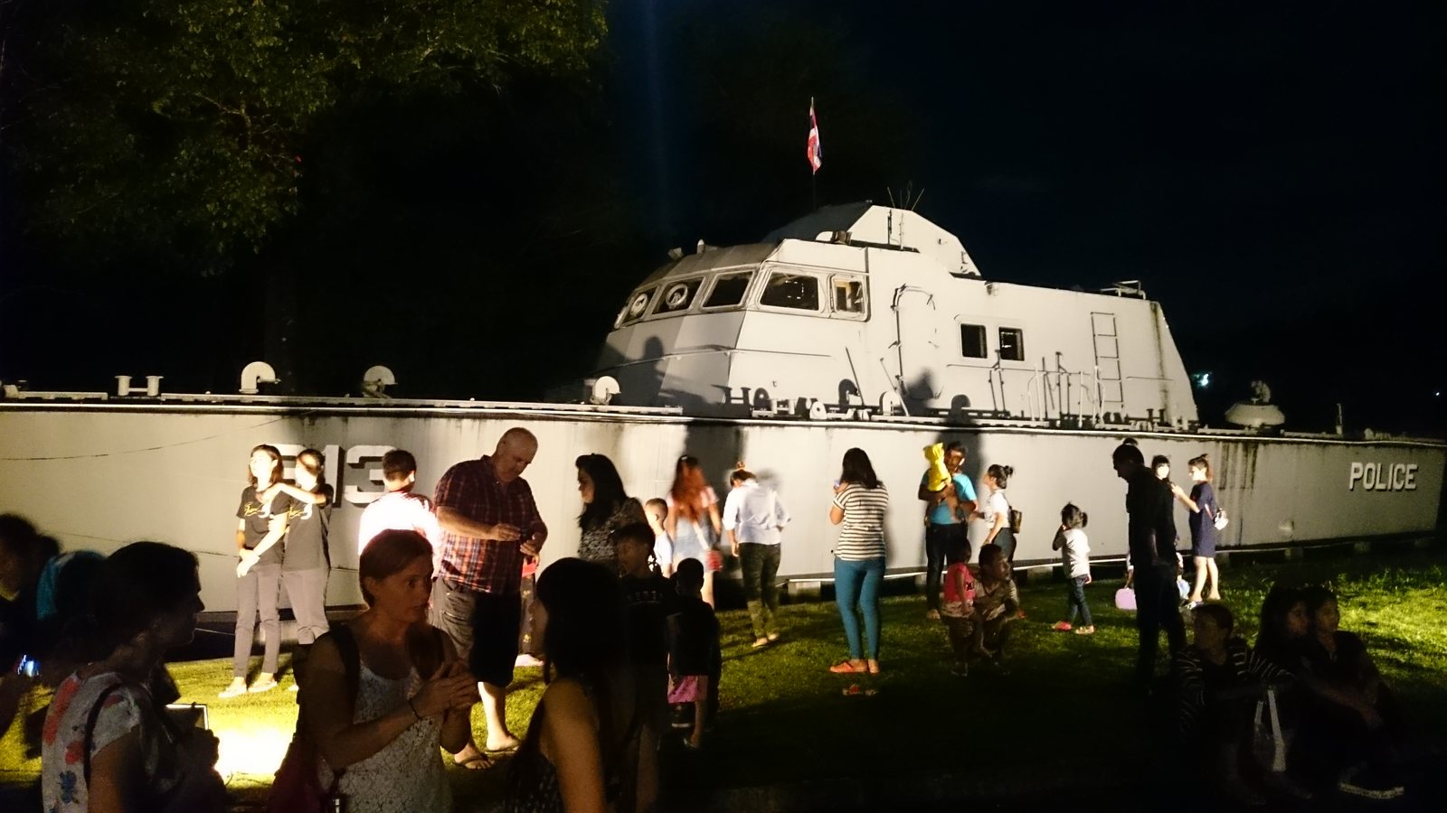 A grey police patrol boat standing on land among trees, with a memorial plaza around it
