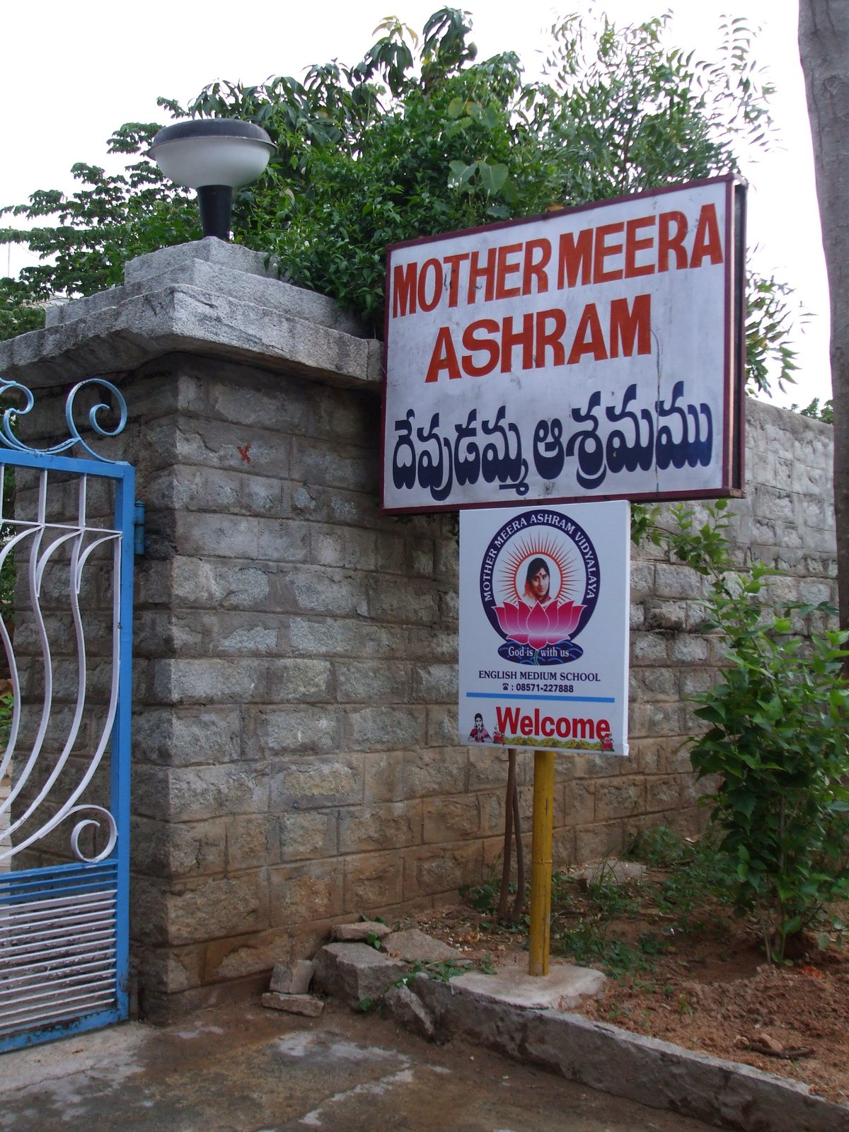 The stone gate of the Mother Meera ashram in Andhra Pradesh, with painted signs for the ashram and its English-medium school.