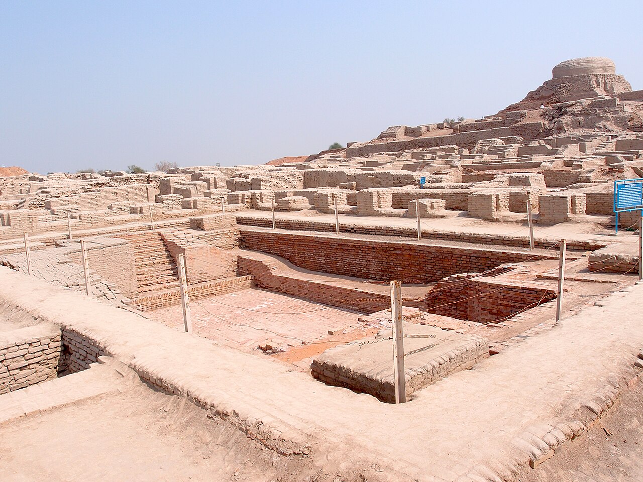 Excavated brick streets and buildings at Mohenjo-daro with the Buddhist stupa on the mound behind.
