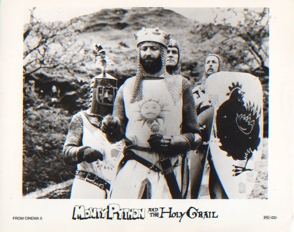 Black and white 1974 publicity still: four Monty Python members in chain mail as knights, King Arthur in the centre wearing a crown