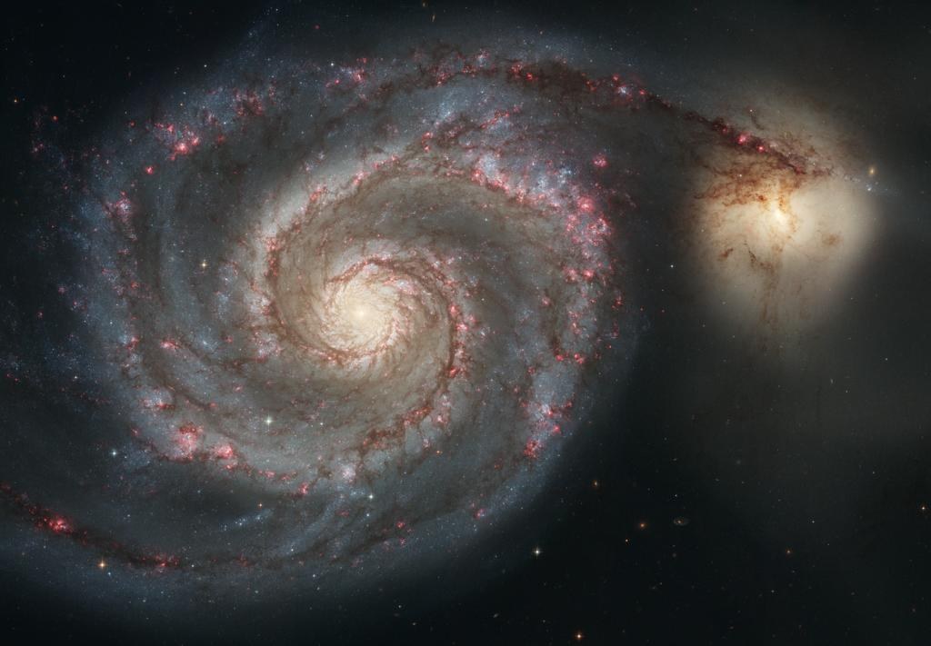 The Whirlpool Galaxy: a face-on spiral with pink star nurseries along its arms, beside a smaller golden galaxy